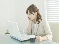 頬杖を突きながらパソコンで作業している女性